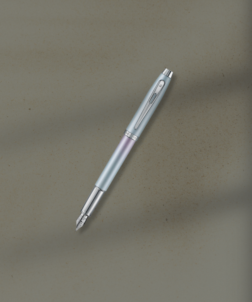 Slanted fountain pen with a silver nib on a textured beige surface, gradient barrel in pale blue and lavender colors.