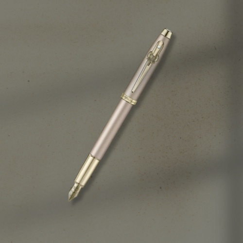 Pink fountain pen with gold trim and clip, angled diagonally on a textured beige surface.