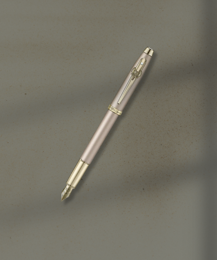 Pink fountain pen with gold trim and clip, angled diagonally on a textured beige surface.