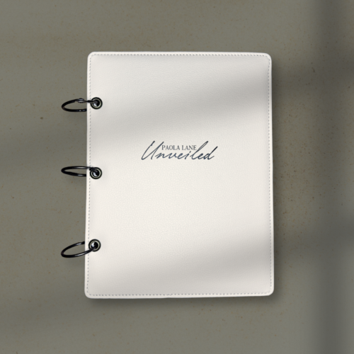 White leather binder with three metal rings on a beige surface; cover shows 'Paola Lane Untitled' in cursive.