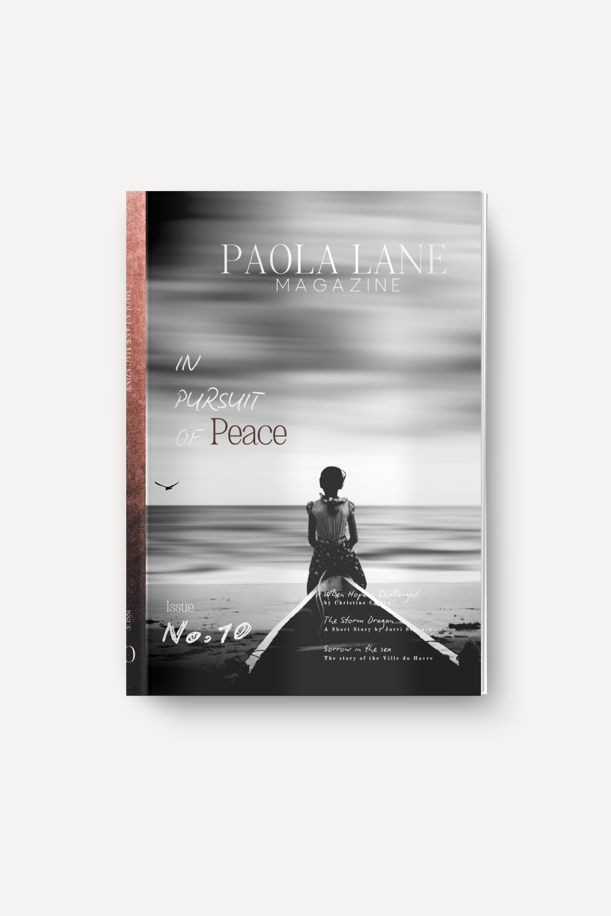 Cover of Paola Lane Magazine with a black-and-white seascape; a person sits on a boat at the shore beneath a cloudy sky, text reads 'Paola Lane Magazine' and 'IN PURSUIT OF Peace' (Issue No.10).