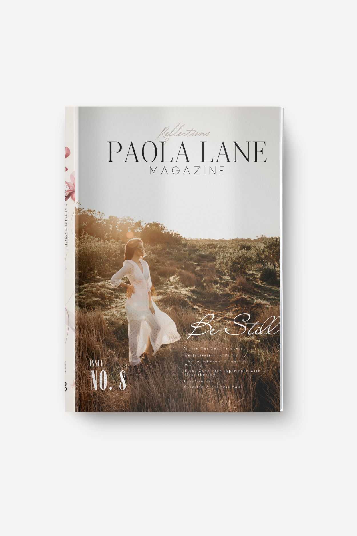 Magazine cover for Paola Lane Magazine with the title 'Reflections' and a woman in a white dress standing in a sunlit field; warm golden hour light washes over grass and shrubbery.