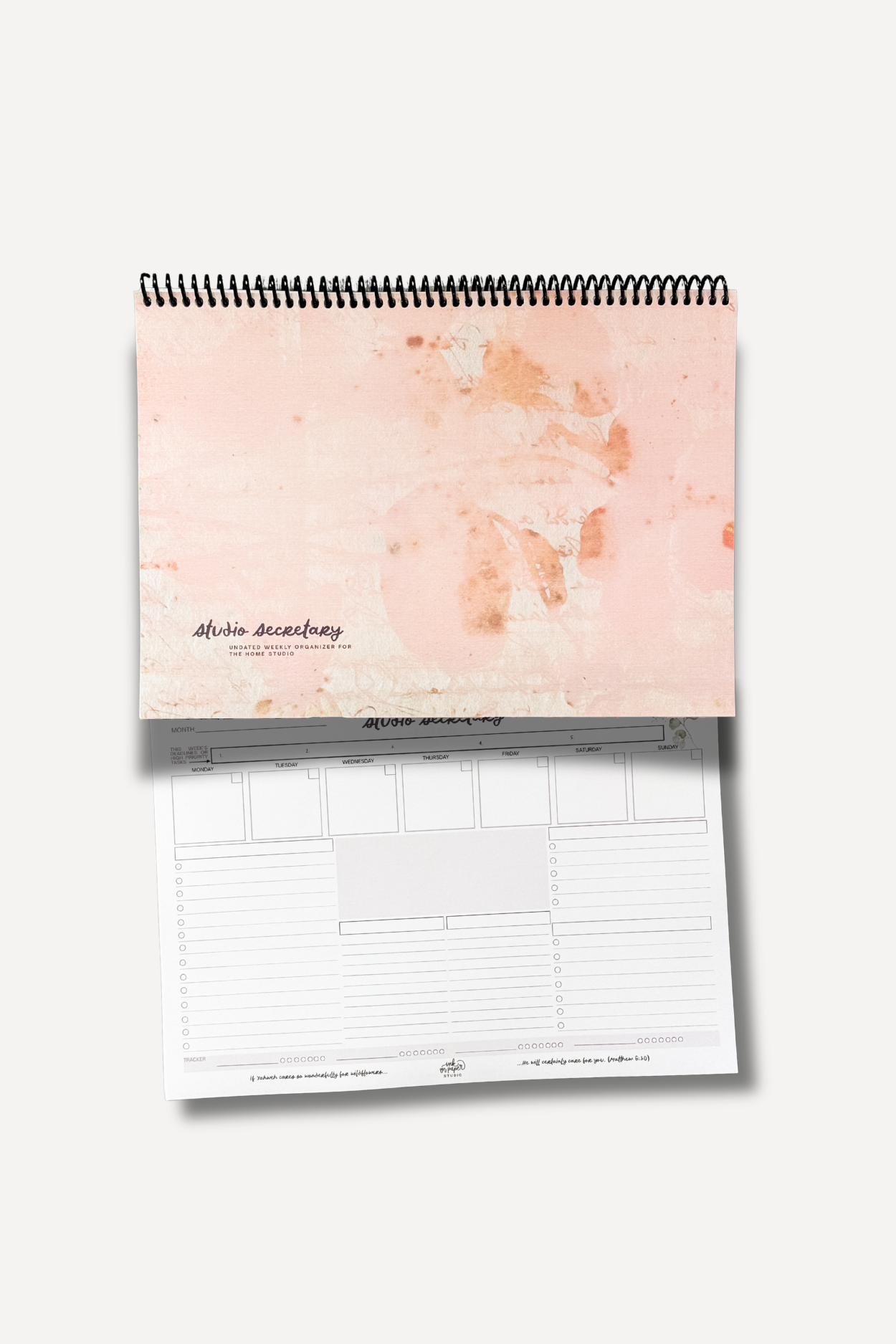 Pink spiral-bound notebook with a stained pink cover resting on top of a weekly planning sheet titled 'studio secretary'.
