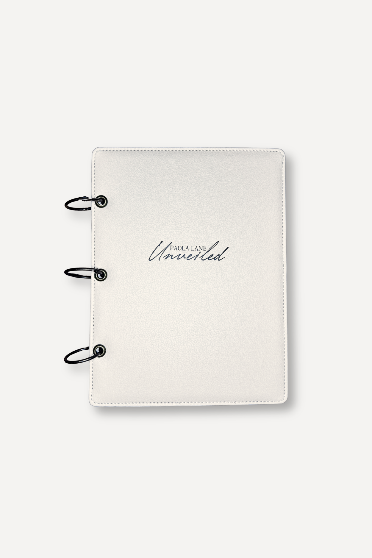 White textured binder with three metal rings along the left edge, displaying the logo 'Paola Lane Unveiled' on the cover.